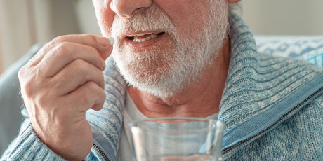 man op leeftijd houdt een pil en een glas water vast