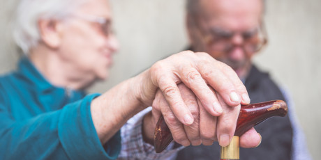Bejaard stel, man houdt een wandelstok vaste en zijn vrouw heeft haar hand op die van hem gelegd