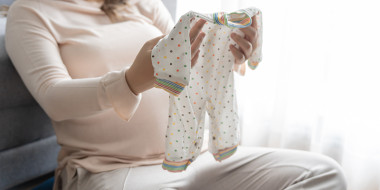 Zwangere vrouw houdt babykleertjes vast
