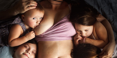 Moeder, liggend, met 4 kleine kinderen van wie er eentje nog borstvoeding krijgt