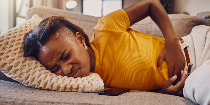 Vrouw met vertrokken gezicht en handen op de onderbuik liggend op de bank